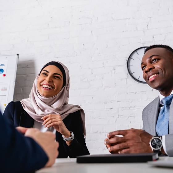 excited arabian businesswoman laughing during meeting with african american business partner and interpreter, blurred foreground